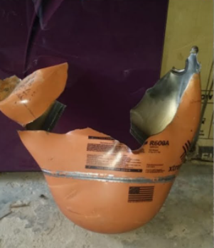 Crushed orange plastic container with black scuff marks on a concrete floor near a wall.