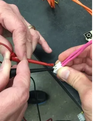 Hands wiring red and pink cables into a small white connector on a workbench