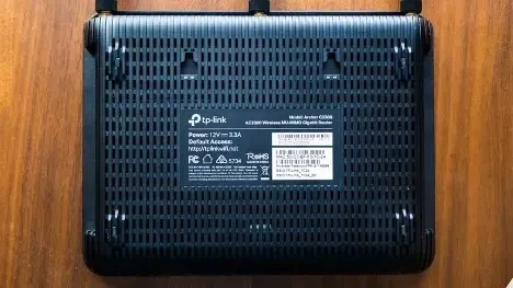 Bottom view of a black TP-Link router with label, resting on a wooden surface.