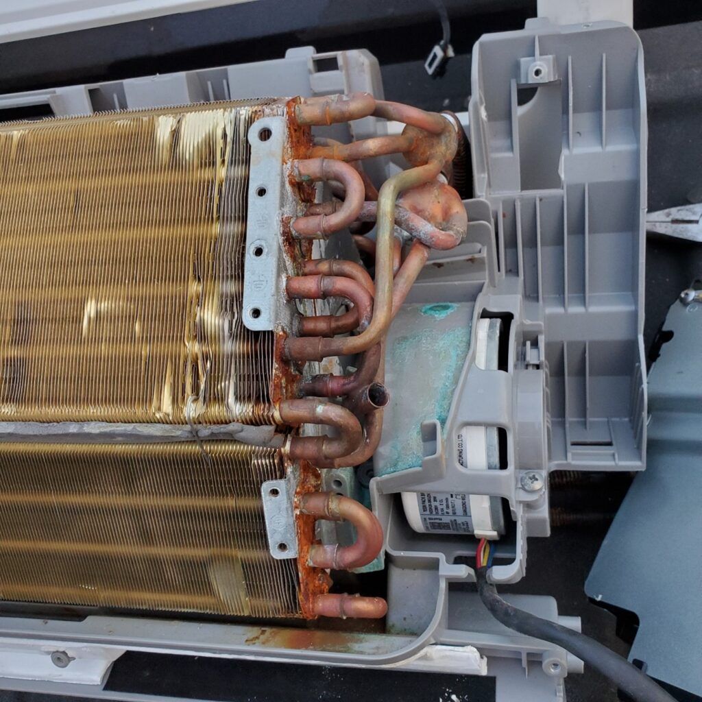 Close-up of a dirty HVAC evaporator coil with copper tubing and gray plastic housing.
