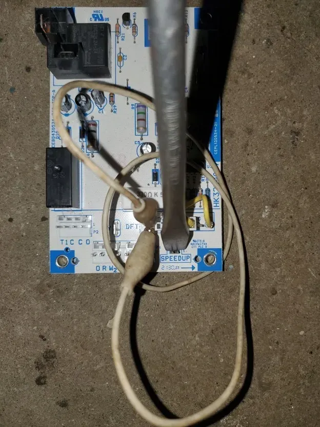 Close-up of a wall-mounted circuit board with connected wires and a vertical metal pipe.