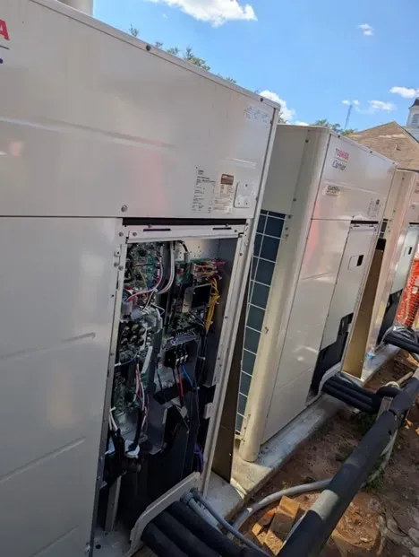 Open electrical panels on rooftop HVAC units with exposed wiring and conduit.