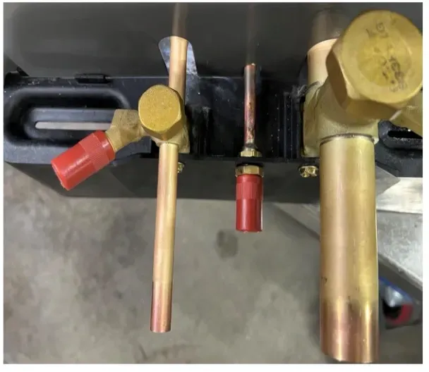 Close-up of brass valves and copper pipes with red handles on a dark machine panel.