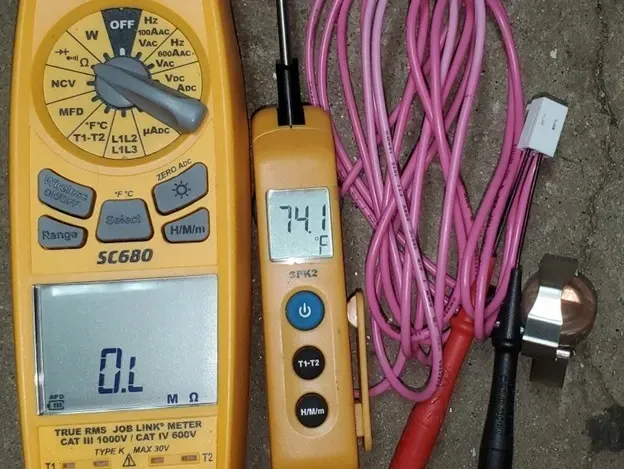 Yellow digital multimeter, yellow thermometer probe, and pink cables arranged on a surface.