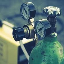 Close-up of a green oxygen tank with two pressure gauges and valves attached