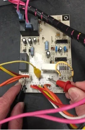 Close-up of hands probing a circuit board with red and yellow test leads and wires.