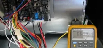Electrical wiring inside a machine cabinet next to a yellow digital multimeter displaying a reading