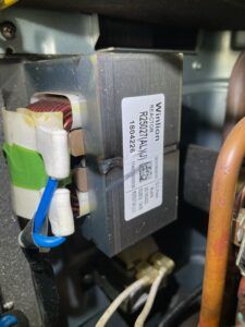 Close-up of an electrical component with wires and a label inside a metal appliance.