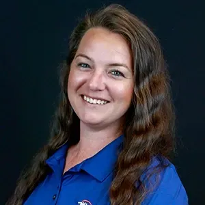 Smiling woman in blue collared shirt against a dark background