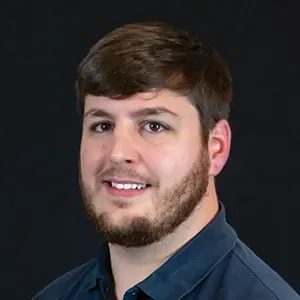 Portrait of a smiling man with brown hair and beard on a dark background