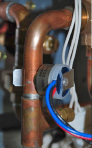 Copper pipe with a small gray valve and blue/red wires in a utility space