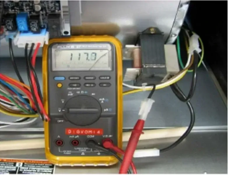 Digital multimeter reading 117.0 volts inside an electrical panel with wires and test leads