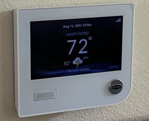 Digital wall thermostat display showing 72°F with weather info on a white wall panel.