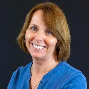 Smiling woman in a blue shirt against a dark background