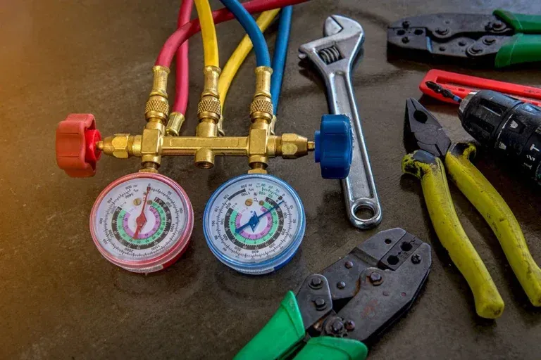 HVAC manifold gauges with colored hoses and assorted wrenches and pliers on a workbench