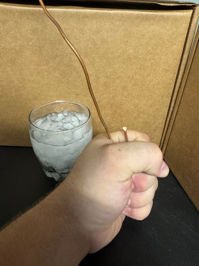 Hand holding a cigarette lighter near a glass of ice water against a gold cushion backdrop