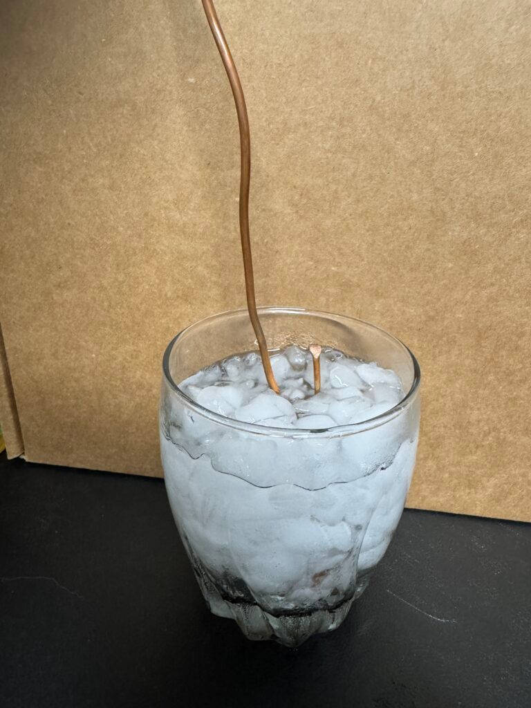 A glass of ice water with a straw on a dark table against a tan background.