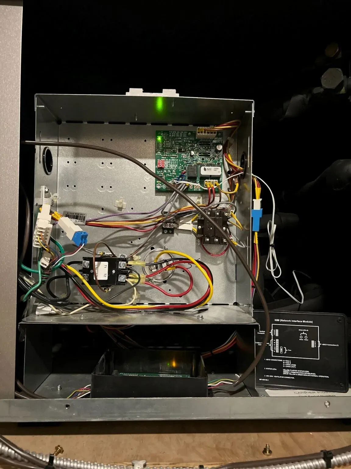 Open metal electronics enclosure with circuit boards, wires, and a green status LED on a workbench