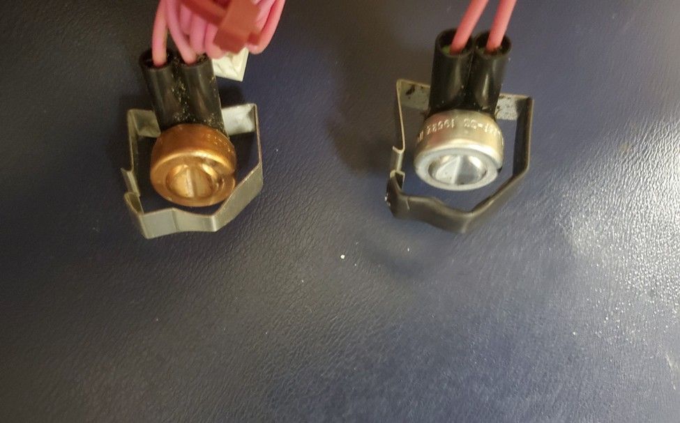 Close-up of two small connector plugs, one gold and one silver, on a dark surface.