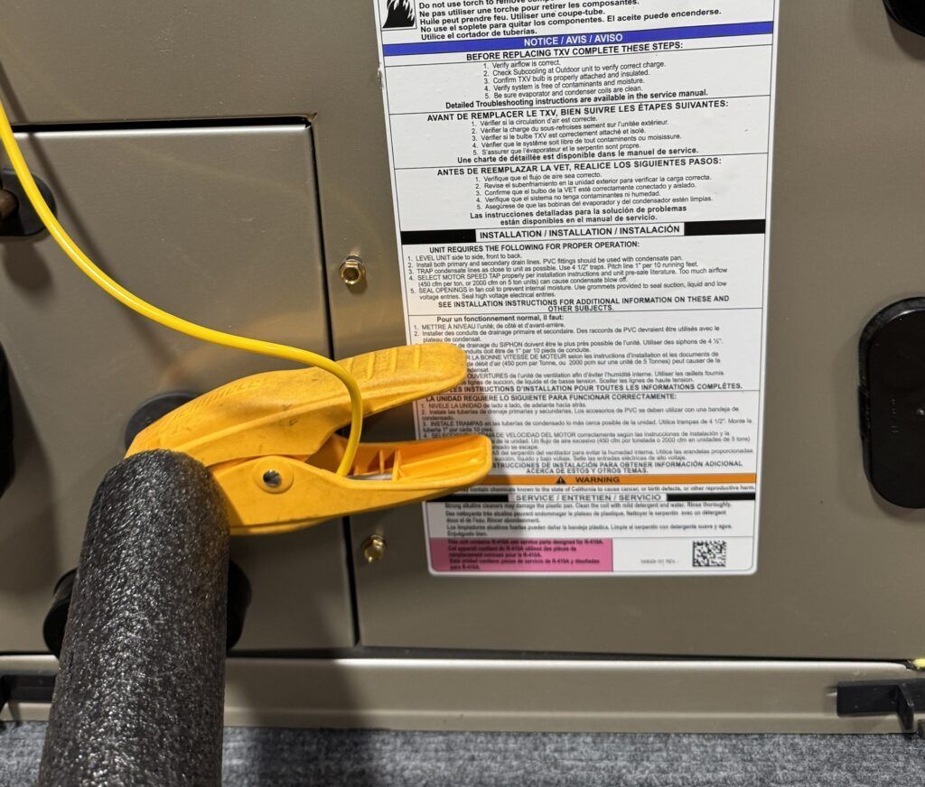 Yellow grounding clamp attached to a gray electrical panel beside a safety instruction label.