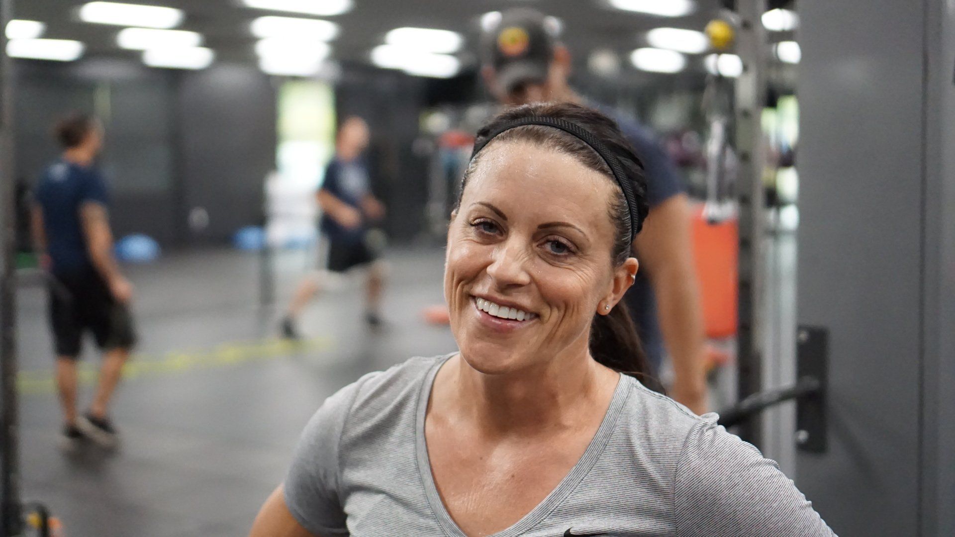 A woman is smiling in a gym with people in the background.