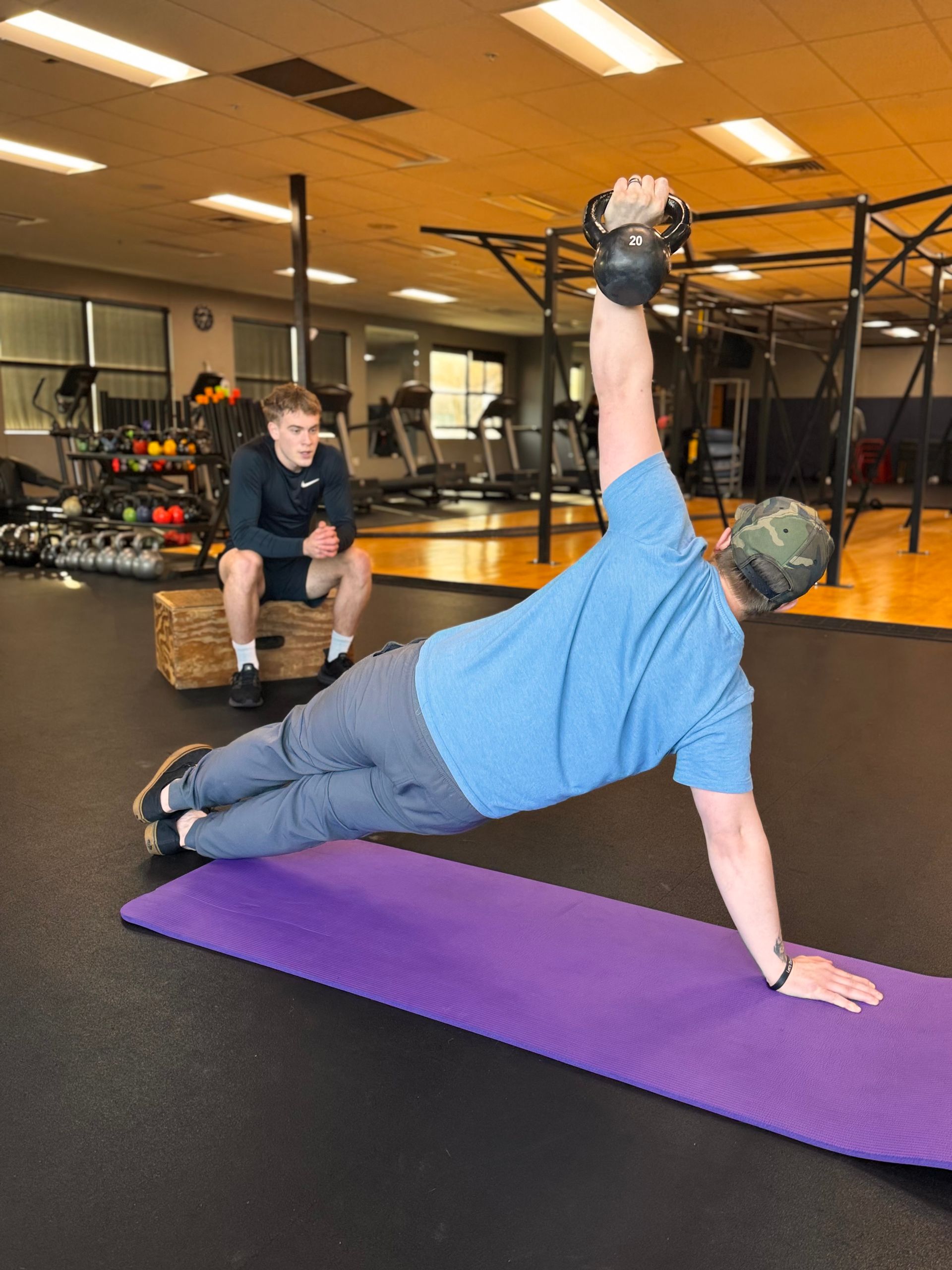 A man is doing a plank on a purple mat in a gym
