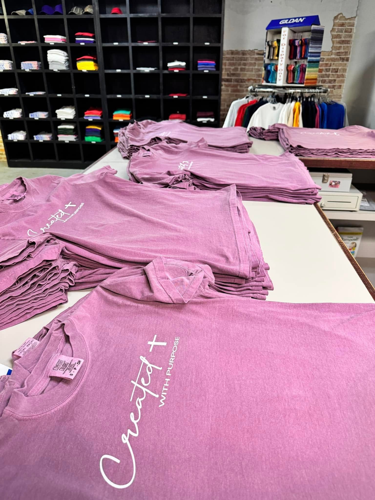 A bunch of purple t-shirts are stacked on top of each other on a table.