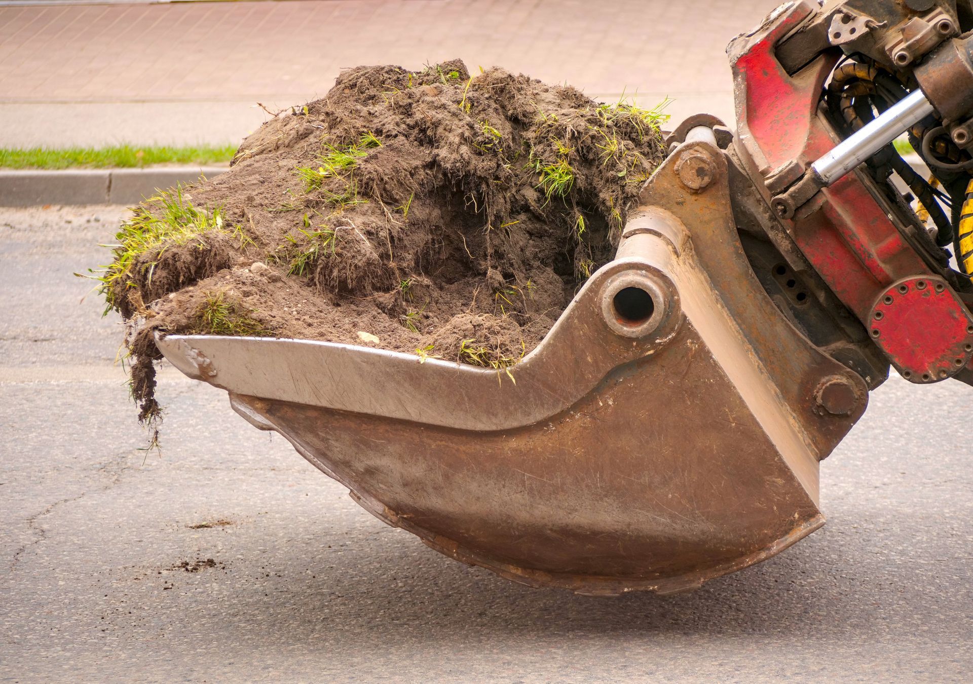 Excavator bucket lifting a clump of dirt and grass beside a paved road