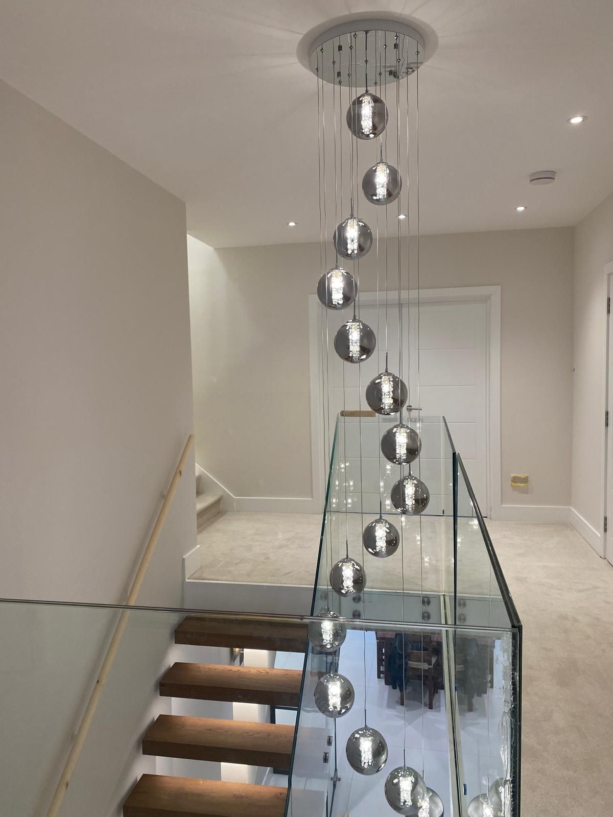 Modern stairwell with glass railing and hanging chrome pendant lights in a bright hallway