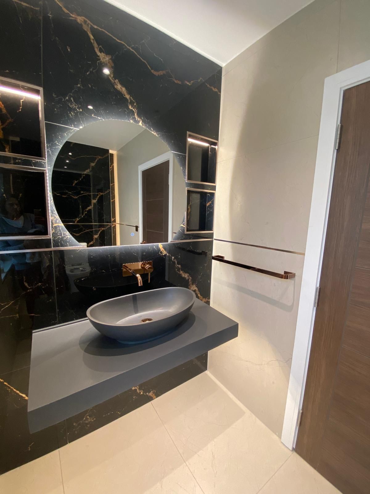 Modern bathroom vanity with black marble wall, round sink, mirror, and wooden door