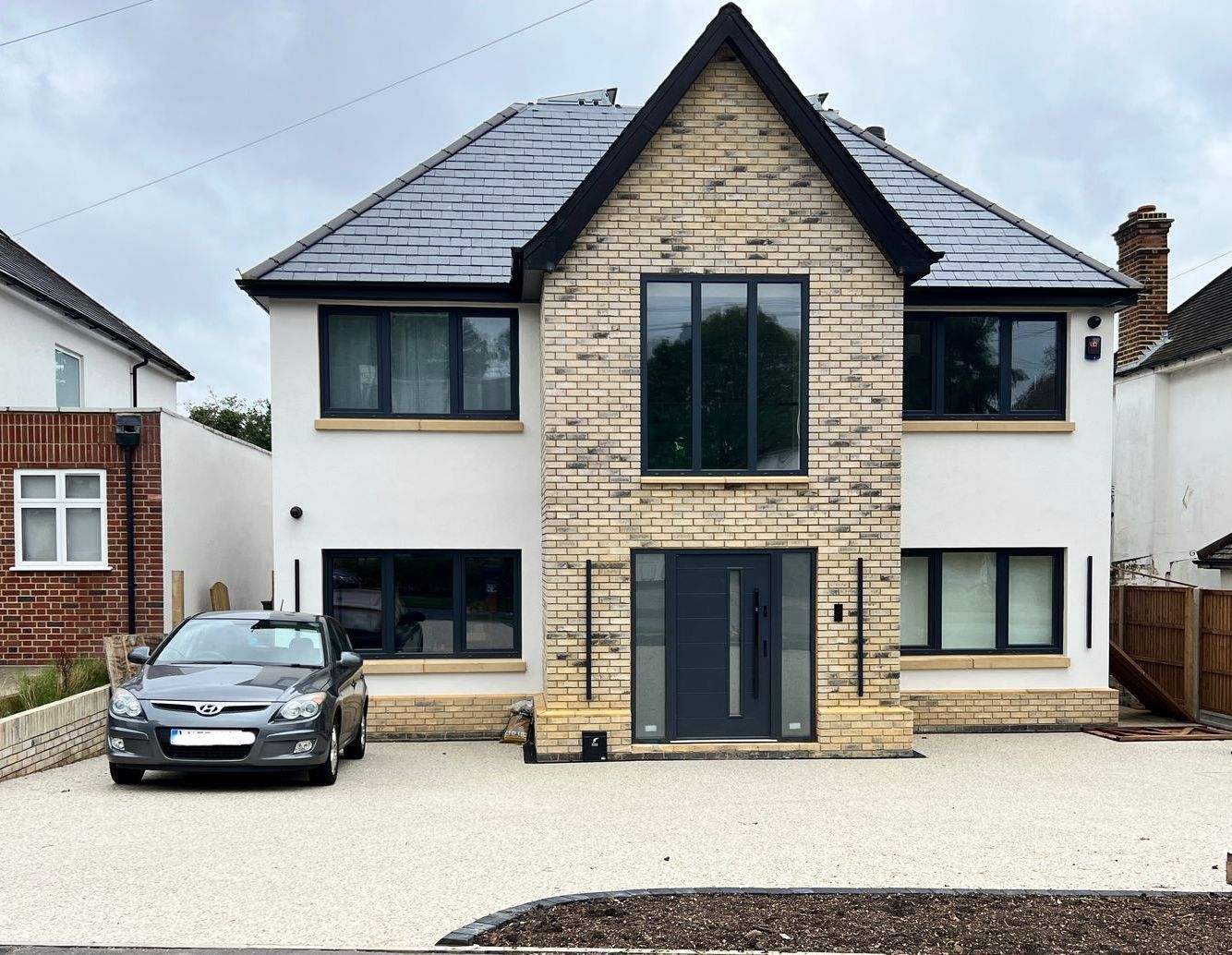 Modern two-story house with stone facade, dark roof, and parked car in the driveway