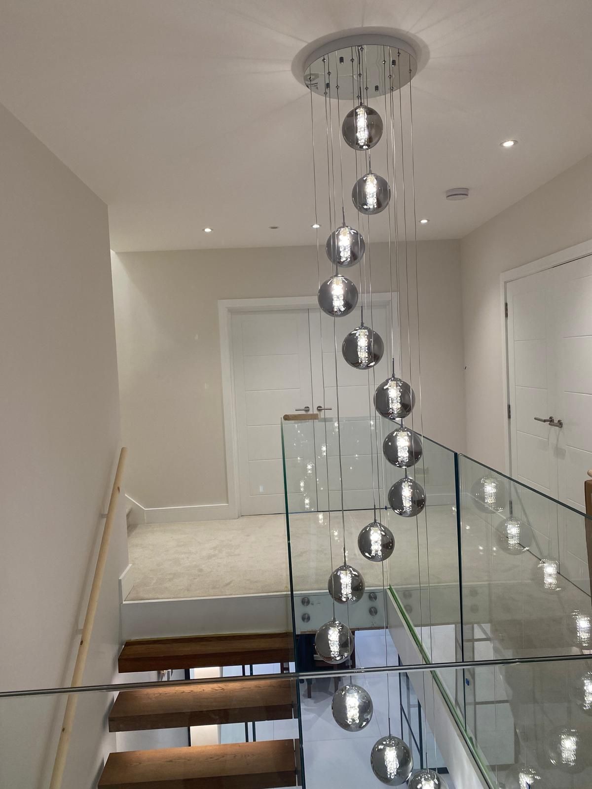 Modern stairwell with glass railing and hanging spherical pendant lights in a bright white interior