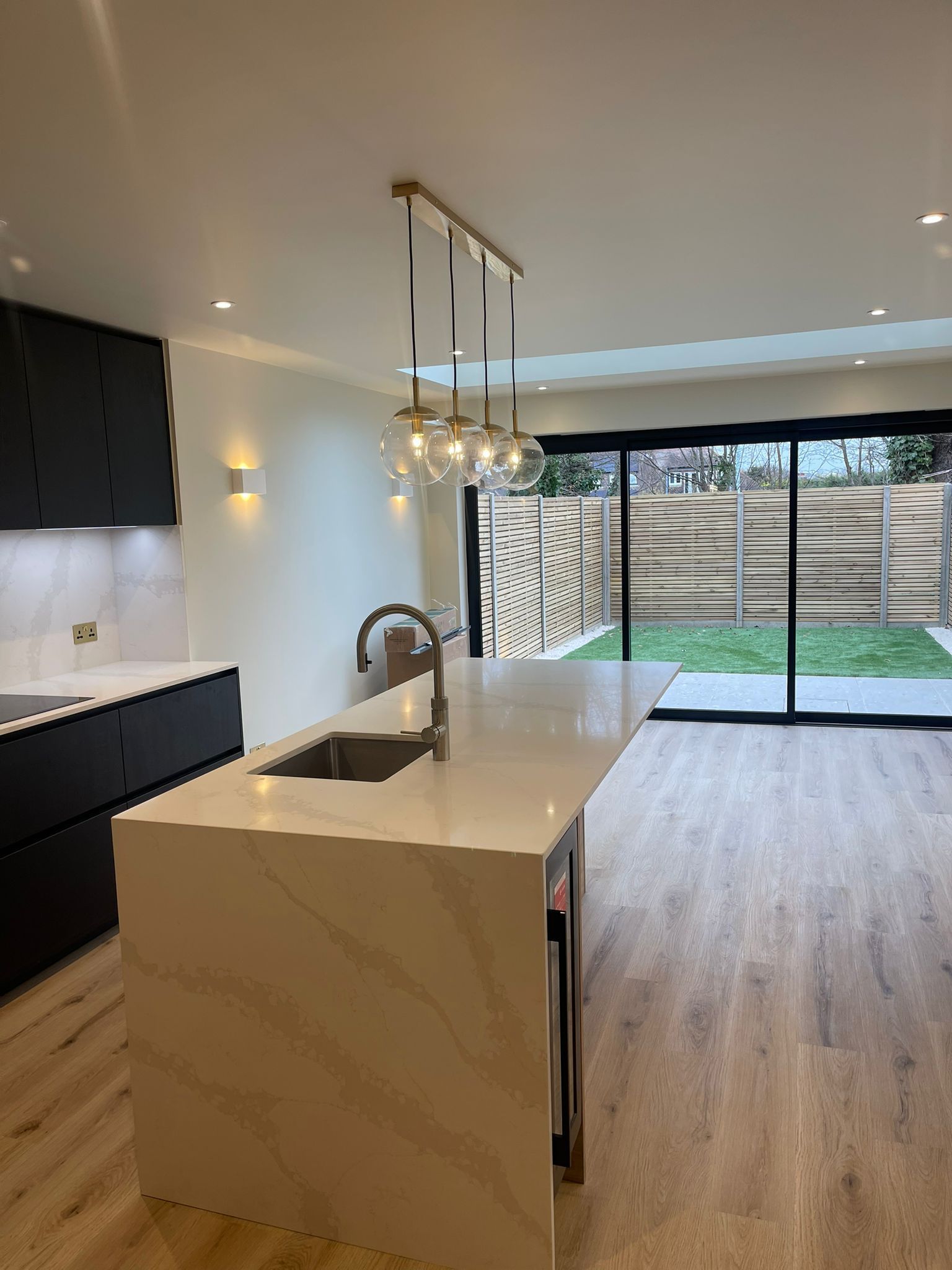Modern open-plan kitchen with island, white counters, dark cabinets, and sliding doors to a patio and yard