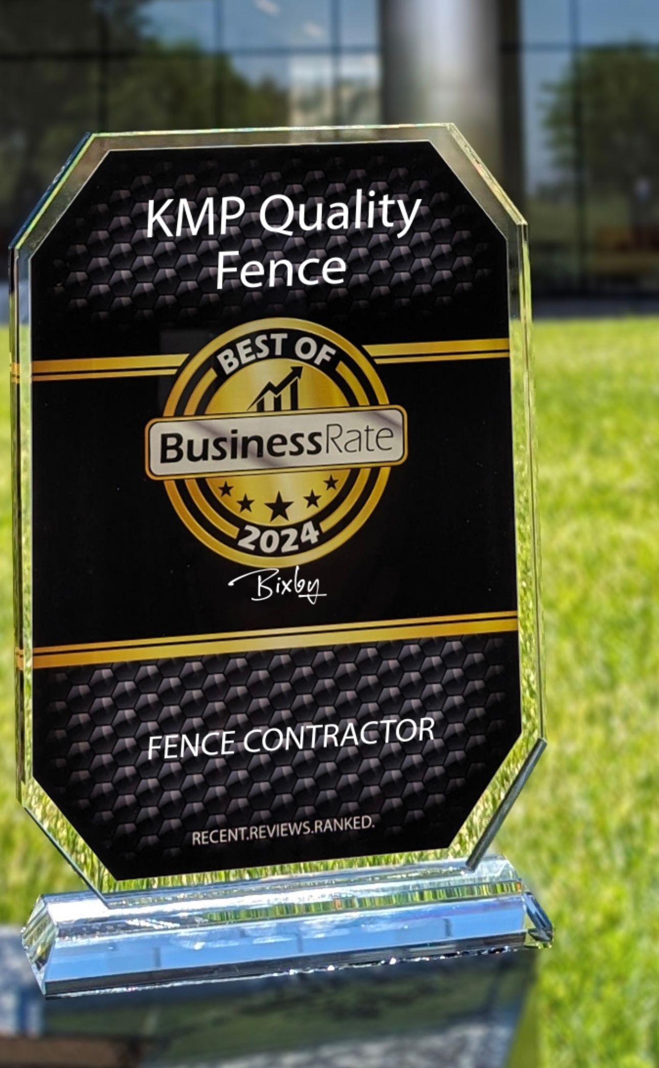KMP Quality Fence “Best of BusinessRate 2024” award plaque on a blue base outdoors