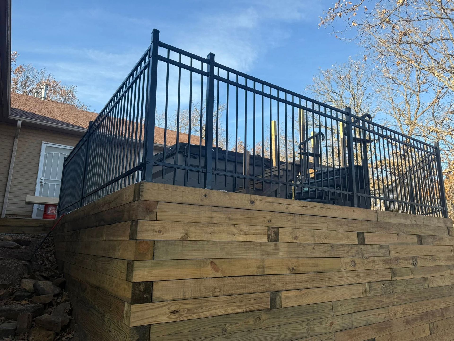 Blue metal railing on a raised wooden deck in a backyard under a clear sky