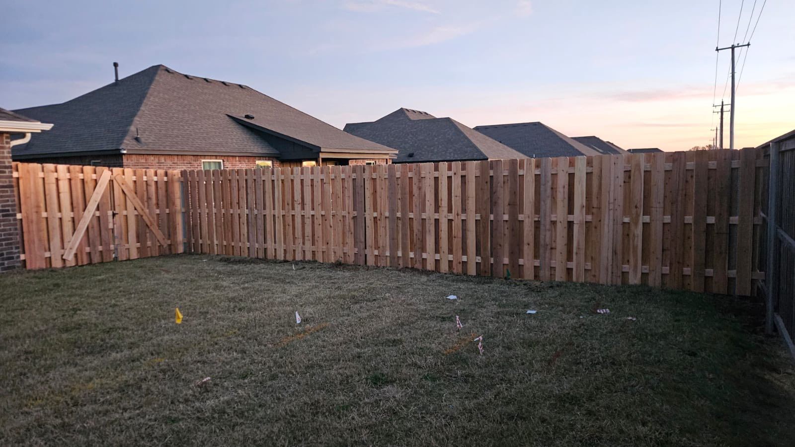 Backyard with a wooden privacy fence, grassy lawn, and suburban houses at sunset