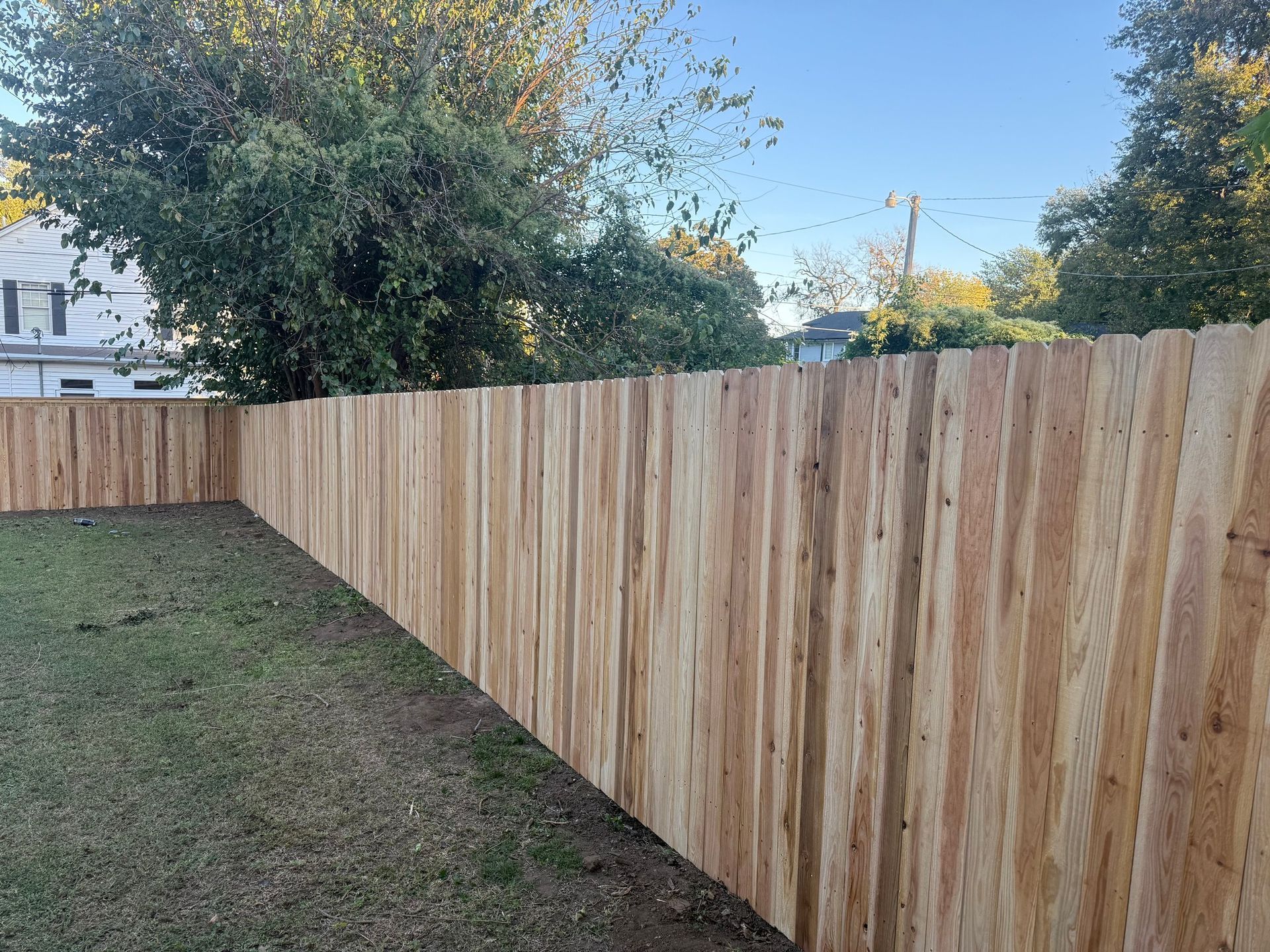 Backyard with a newly built wooden fence beside a grassy lawn under a clear sky