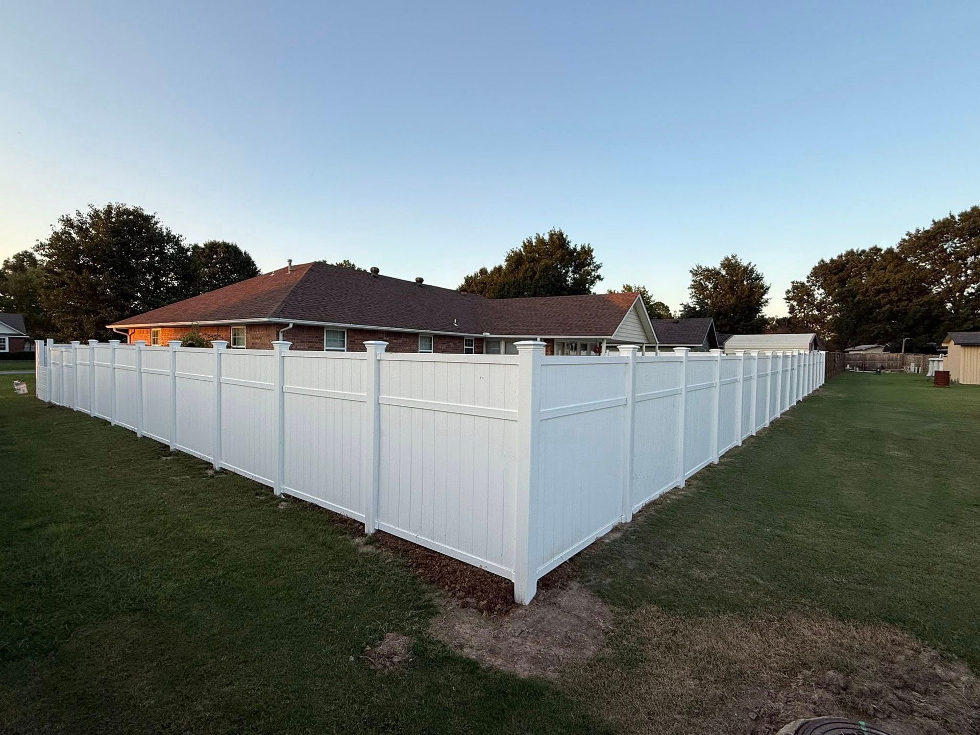 White vinyl fenced yard around a red-roofed house at dusk