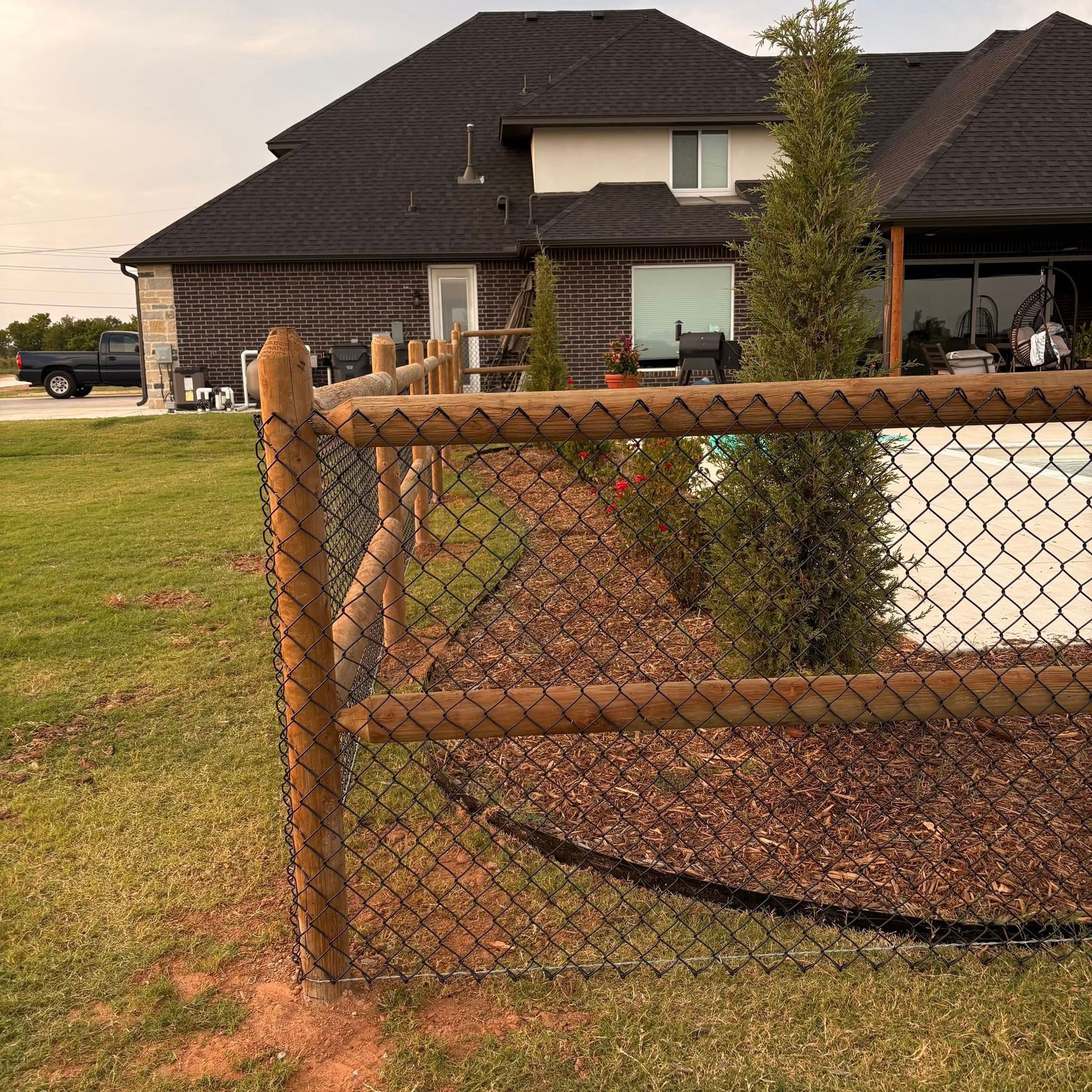 Backyard with chain-link fence, landscaped yard, and a large two-story house at sunset.