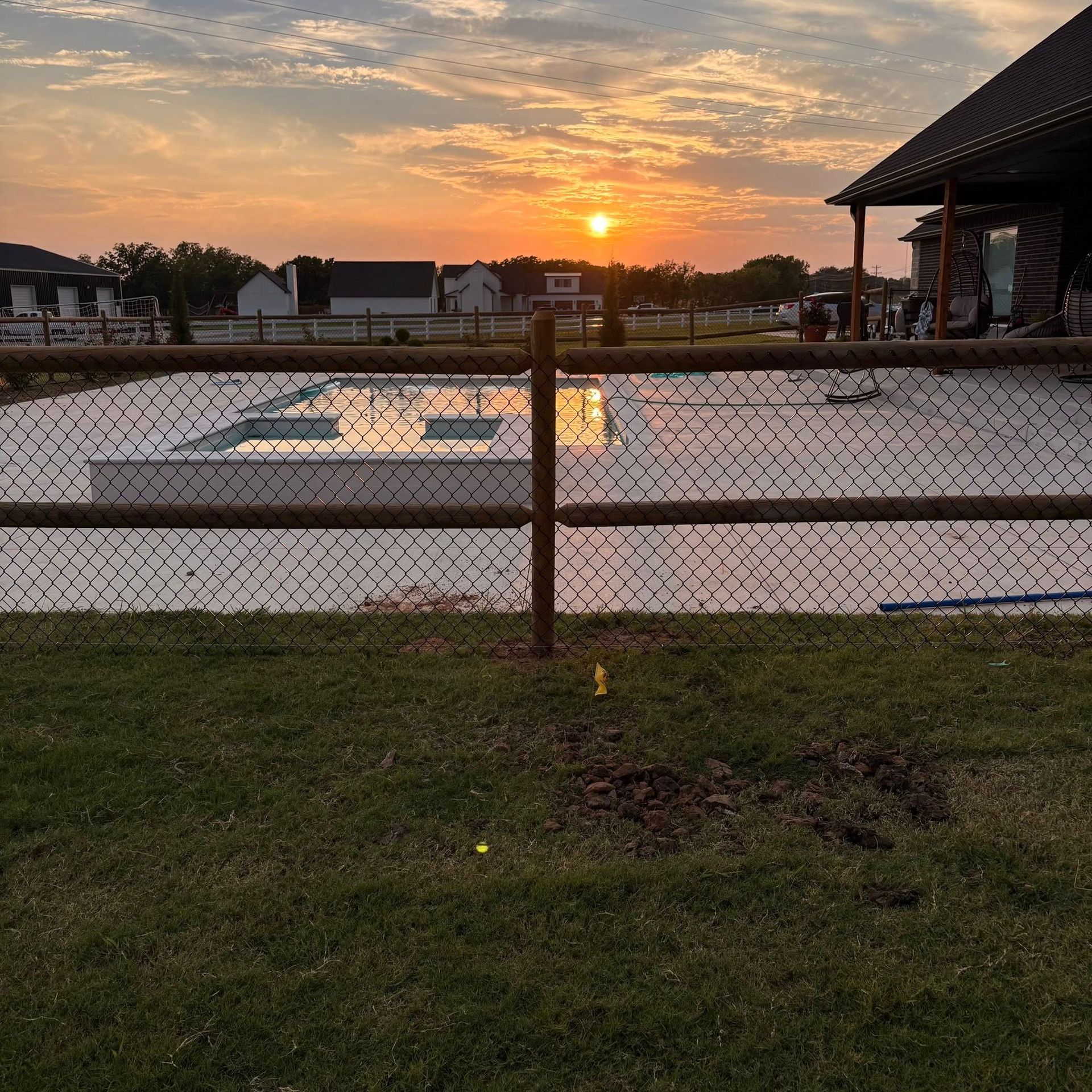 Sunset over a fenced pool area with a reflective pool and grassy foreground