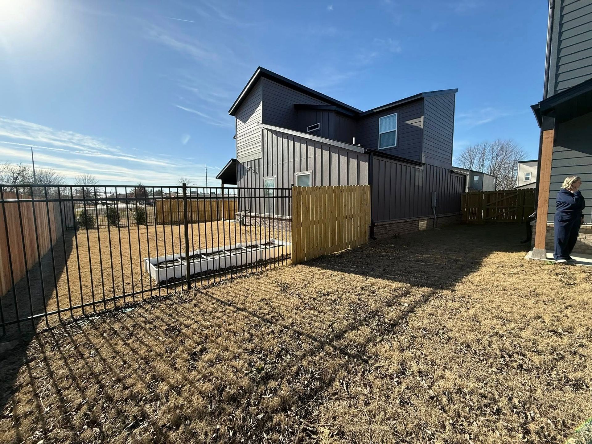 Backyard with a fenced yard, gravel ground, and a modern house under a blue sky