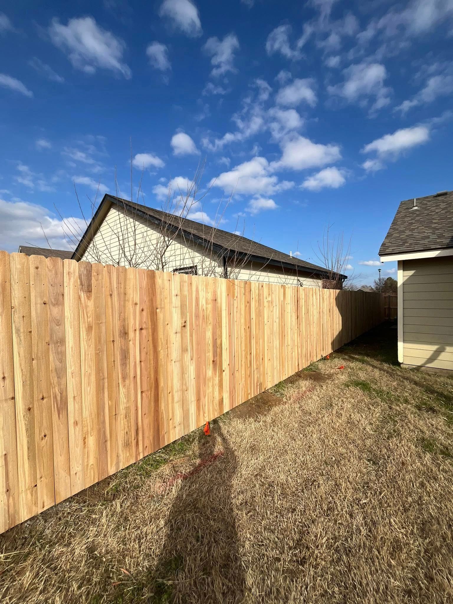 Wooden fence in backyard, sunny day with house and shed visible.