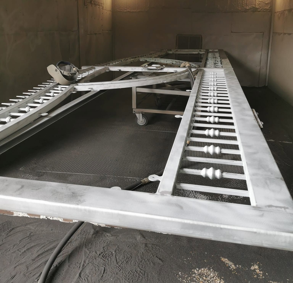 Operai con tute protettive puliscono a spruzzo attrezzature metalliche industriali in un locale di fabbrica.