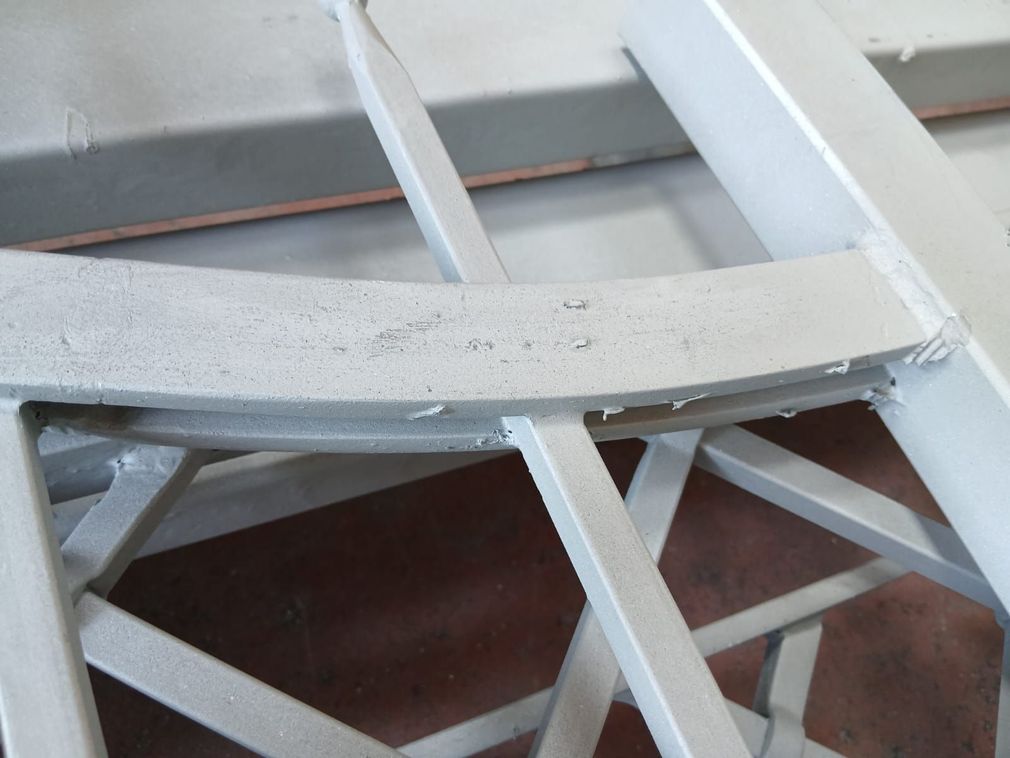Un operaio in tenuta antisommossa spruzza acqua su una recinzione in ferro decorata, pulendola da ruggine e polvere in un ambiente simile a un'officina.