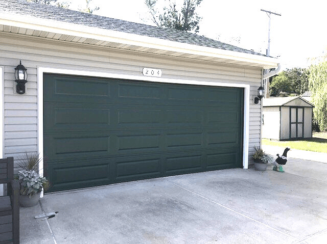 Dark green garage door on a house with a driveway and small shed nearby.