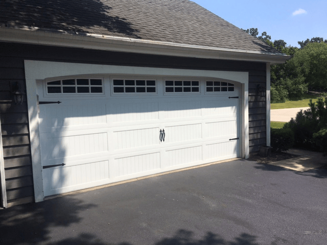 White two-car garage with a paneled door beside a driveway under a shingled roof.
