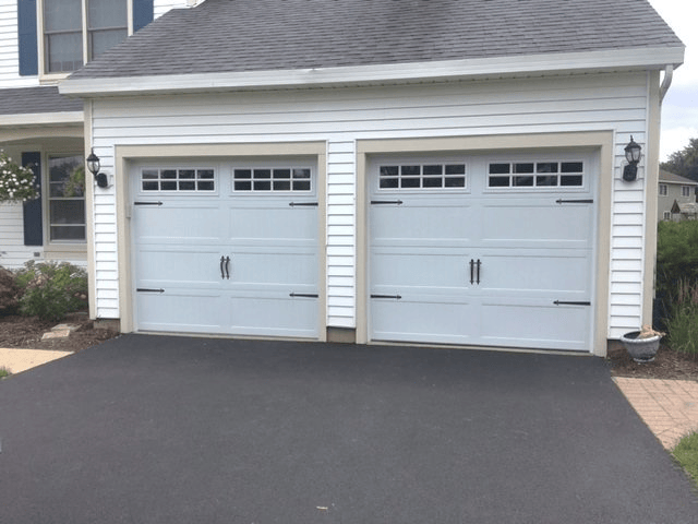 Two light blue garage doors on a white house with a dark asphalt driveway