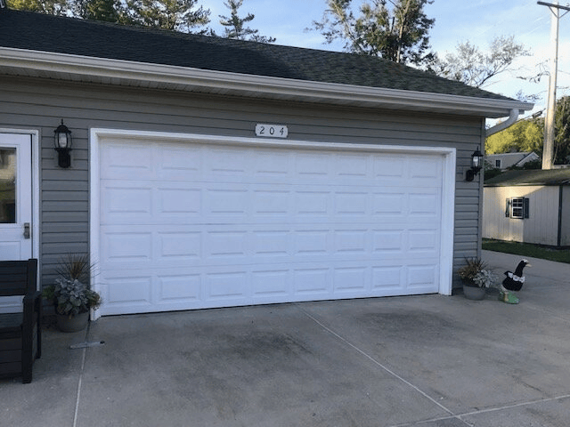 White double garage door on a gray house with driveway and a small dog at the right edge.