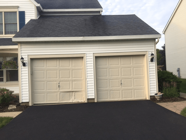 Two-car beige garage with dark shingled roof and black driveway