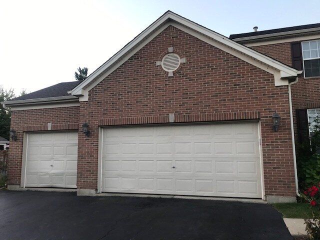 Two-car brick garage with white doors and a black driveway